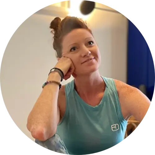 Die "Yoganomadin" sitzt in einem Yogaraum auf der Matte und lächelt ihr Gegenüber an.